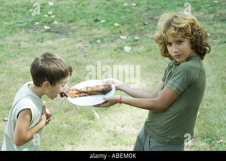 Boy holding up assiette de grillades tandis que le second garçon se penche en avant pour prendre des en-cas Banque D'Images