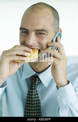 Man eating hamburger and using cell phone Banque D'Images