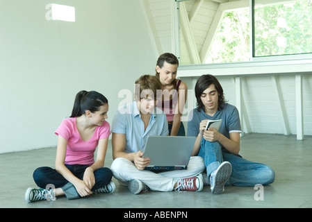 Quatre amis adolescents assis sur le plancher, à l'aide d'ensemble ordinateur portable Banque D'Images