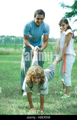 L'extérieur de la famille, père et sœur holding jambes du garçon comme brouette Banque D'Images