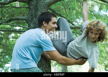 Boy climbing tree, père l'attraper Banque D'Images