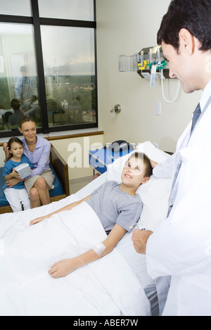 Boy lying in hospital bed, entourés de leur famille et médecin Banque D'Images