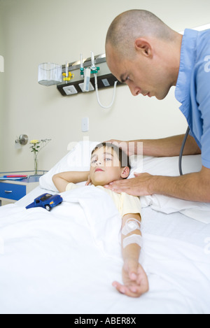 Boy lying in hospital bed, médecin taking pulse Banque D'Images