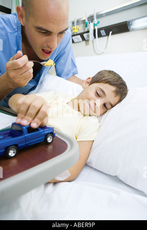 Boy lying in hospital bed, médecin encourageant à manger garçon Banque D'Images