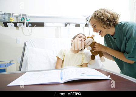 Boy lying in hospital bed, se blottissant avec toutou infirmière est tenue en place Banque D'Images