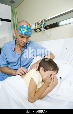 Boy lying in hospital bed, médecin à l'écoute de dos du garçon avec stéthoscope Banque D'Images