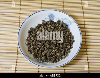 Perles de jasmin thé de Chine dans un bol sur un tapis de bambou Banque D'Images