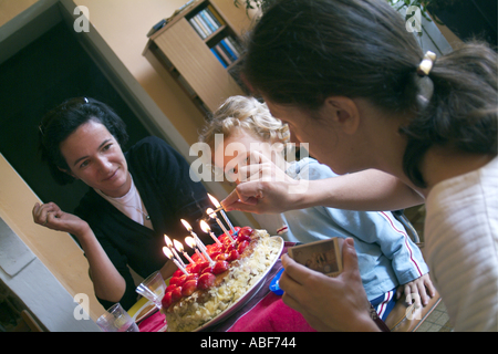 Mère, tante et sœur foule autour de la table pour allumer les bougies pour célébrer l'anniversaire d'un garçon de neuf ans. Banque D'Images