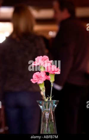 Fleur oeillet rose dans un pub sur une table avec deux personnes dans un bar à discuter avec les autres Banque D'Images