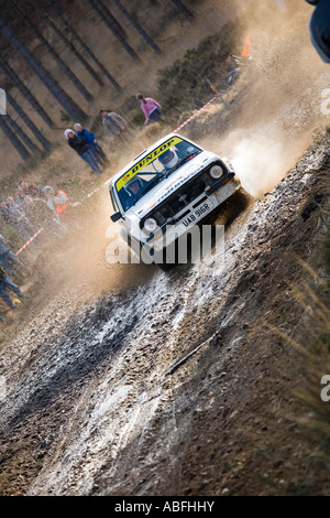 Ford Escort blanche voiture rallye action conduite des cailloux de pulvérisation la pulvérisation de terre et de boue flaque eau comme il tourne un coin Banque D'Images