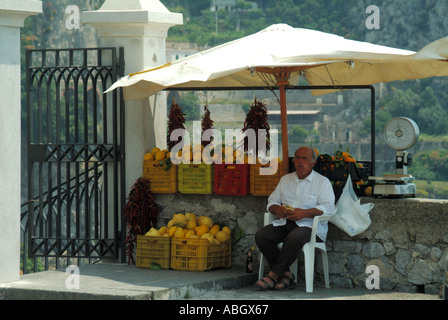 Homme de route côtière d'Amalfi assis sous parasol à un étal vendant des fruits au point d'arrêt pour des excursions touristiques en autocar faisant côte du golfe de Salerne UE Banque D'Images