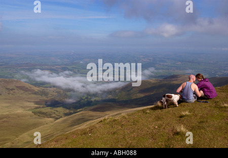 Les randonneurs s'asseoir sur le sommet du Pen Y Fan avec leur chien épagneul paysage avec vue sur la vallée de la brume en Powys South Wales UK Banque D'Images