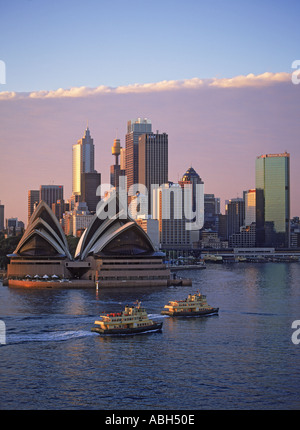 Des taxis bateau traversant le Port de Sydney avec l'Opéra et de la skyline at dawn Banque D'Images