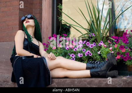 Un Goth girl assis sur un rebord de fenêtre en face d'une planteuse de pétunias Banque D'Images