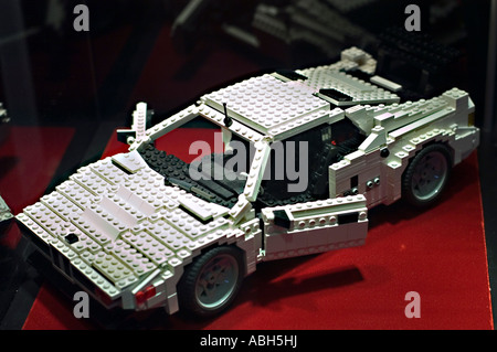 Voiture BMW M1 blanche fabriquée à partir de sets Lego, avec portes ouvertes et détails complexes en briques, affichés sur une surface rouge. Banque D'Images