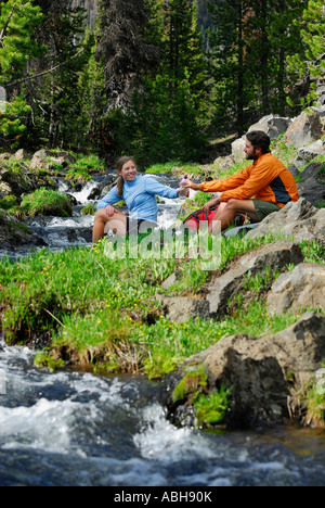 Hiker couple sharing a water bottle cooling down by a rocky mountain stream Banque D'Images