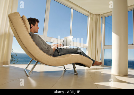 Young man using laptop in armchair Banque D'Images