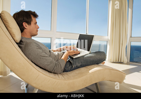 Young man using laptop in armchair Banque D'Images