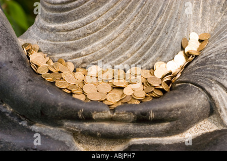 Pièces d'or dans les mains d'une statue de pierre du Seigneur Bouddha méditant à Bodhgaya sous l'arbre Bodhi pour atteindre l'illumination. Banque D'Images