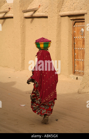 Une femme vêtue de vêtements traditionnels et de transporter un pot sur la tête, passe devant la mosquée Sankoré, Tombouctou, Mali, de l'Ouest Afric Banque D'Images