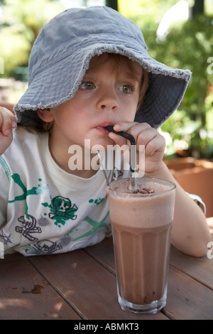 Jeune enfant en été le port floppy chapeau de soleil à la terrasse d'un café avec un grand verre de boisson chocolat glacé avec une paille Banque D'Images