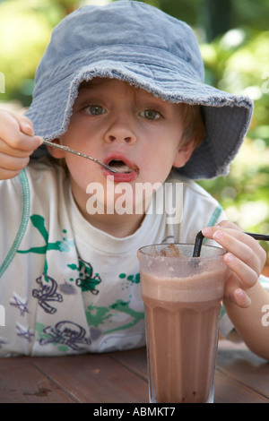 Jeune enfant en été le port floppy chapeau de soleil à la terrasse d'un café avec un grand verre de Chocolat glacé Banque D'Images