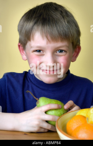 Un garçon de 8 ans assis à une table en train de manger avec poire coupe à fruits Banque D'Images