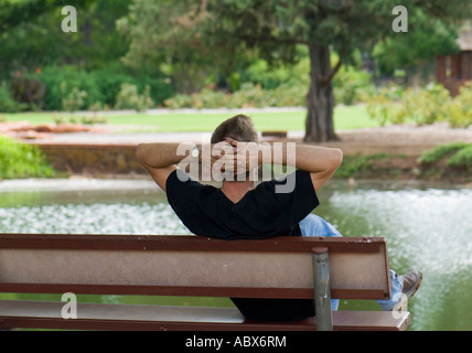 Jeune homme caucasien se remet en marche, se détend, rêve et se déroule assis sur un banc dans un parc à Oklahoma City, Oklahoma, USA. Banque D'Images