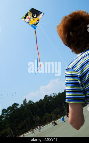 Une femme regarde un cerf-volant coloré planant haut dans le ciel au Hunting Island State Park, Caroline du Sud, États-Unis, par une journée ensoleillée au bord de la plage. Banque D'Images