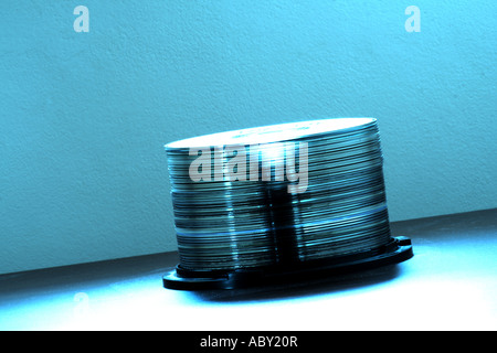 Pile de disques compacts brillants sur un axe en plastique sous un éclairage bleu doux, illustrant les supports de stockage ou l'archivage de données numériques. Banque D'Images