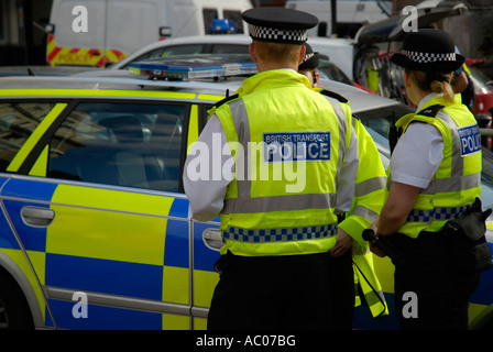 British transport des agents de police de yellow jackets debout à côté de couleur jaune et bleu voiture de police Banque D'Images