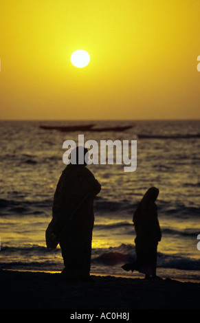 Les femmes mauritaniennes enveloppées de melafas sont silhouetté contre le soleil de l'après-midi à la plage des pecheurs plage des Pêcheurs Banque D'Images