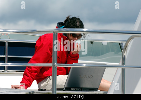 Femme était assise sur le pont supérieur du bateau de croisière à moteur travaillant sur ordinateur portable à Cowes Yacht Haven Isle of Wight angleterre uk Banque D'Images