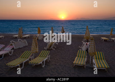 Un coucher du soleil orange chaud sur la mer Egée avec des chaises longues et des parasols sur la plage paniers jusqu'à la fin de la journée. Banque D'Images