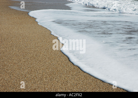 Foam laissés par vague sur la plage de sable grossier Banque D'Images