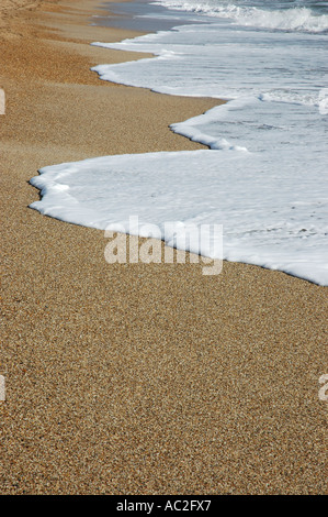 Foam laissés par vague sur la plage de sable grossier Banque D'Images