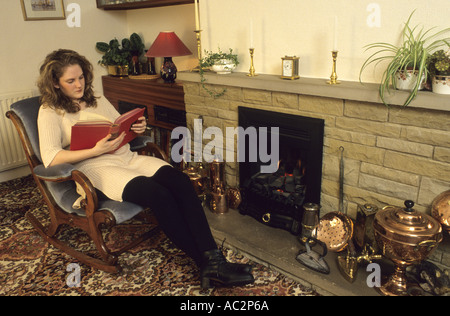 Dame à vous détendre près de la cheminée en lisant un livre dans la maison Banque D'Images