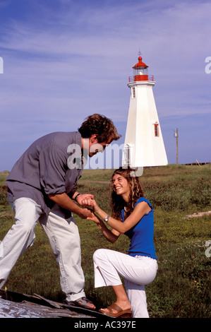 Jeune couple avec phare en arrière-plan l'escalade sur le vieux bateau dans nord-est du Nouveau-Brunswick près de Shippagan Banque D'Images
