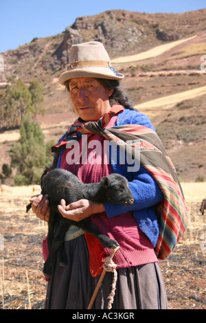 Quechuan bergère vêtu du costume traditionnel aux couleurs vives, et hat holding châle 7-day-old lamb dans Andes près de Urubamba, Pérou Banque D'Images