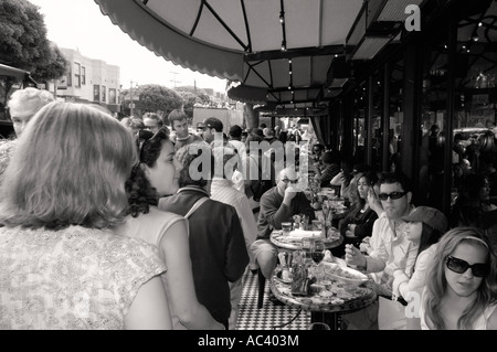 Les gens dînent à de petites tables en plein air sous un grand auvent dans un café urbain bondé en Californie sur cette photographie en noir et blanc. Banque D'Images