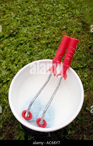 Deux rouleaux de peinture rouge vif trempant dans un seau, qui est rempli d'eau blanche et de mélange de peinture , Finlande Banque D'Images