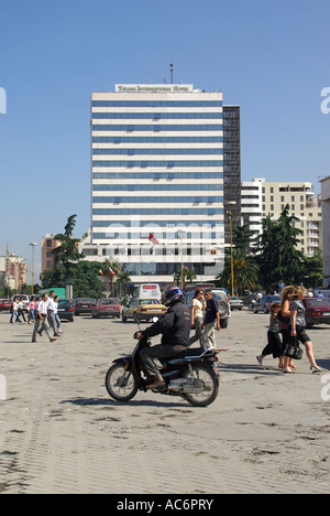 Scène de rue en République d'Albanie Tirana, la place Skanderbeg cyclomoteur en esquivant de poule personnes traversant route multi histoire Tirana International Hotel beyond Banque D'Images