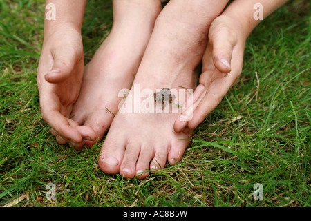 Photo d'un garçon la collecte d'un crapaud perché sur son bébé Pieds sales dans l'herbe Banque D'Images