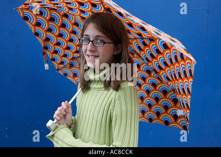 Un onze ans English girl smiling est vêtu d'un tricot vert et cavalier tenant un parapluie de couleur. Banque D'Images