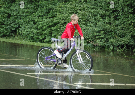 Jeune garçon avec un vélo dans l'eau d'inondation Banque D'Images