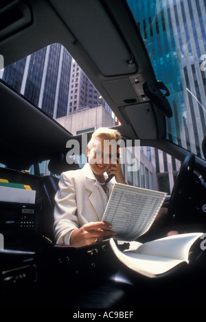 Femme conducteur assis sur le siège avant de la voiture lit des documents et entretiens sur un téléphone cellulaire View of skyscrapers via Windows Banque D'Images