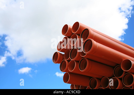 Tuyaux en PVC orange empilés contre un ciel bleu avec des nuages. Banque D'Images