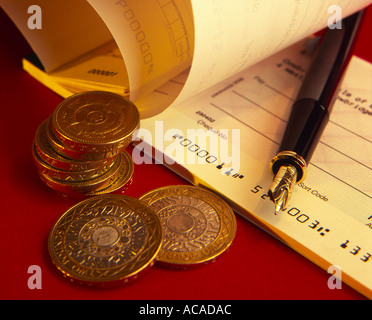 Pièces de monnaie britanniques et stylo carnet de chèques en juxtaposition sur un fond rouge Banque D'Images
