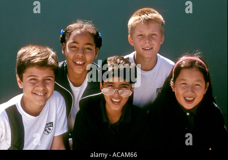 Groupe de société multiraciale happy smiling junior school les élèves à l'extérieur sous le soleil de jeux avec mur derrière sport verte Banque D'Images
