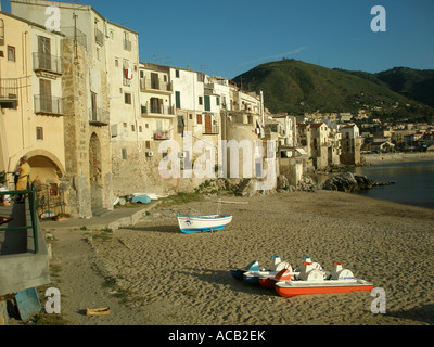 Bateaux et un bateau à pédales sur la plage de sable fin qui lui fait face à la petite ville de Cefalù, sur la côte nord de la Sicile Banque D'Images